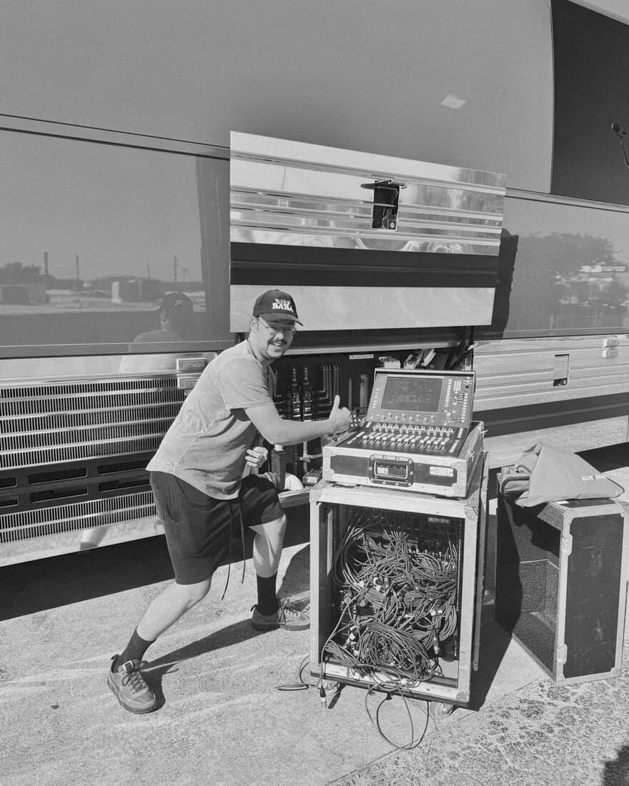 Jacob wheeling a rack of audio gear beside a tour bus